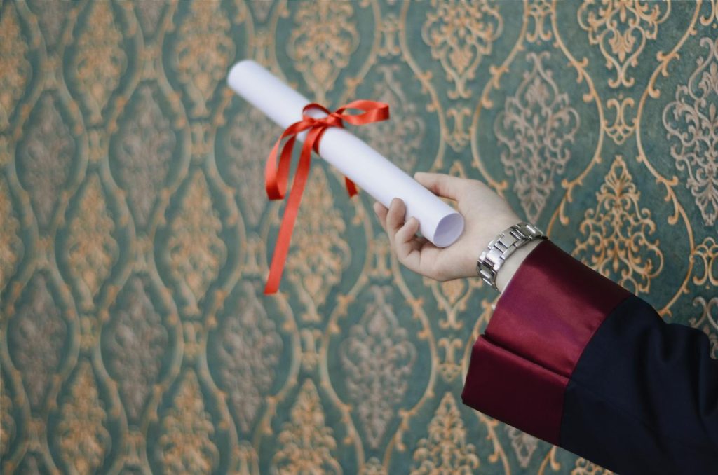 A graduate's hand holding a diploma with red ribbon, symbolizing achievement.